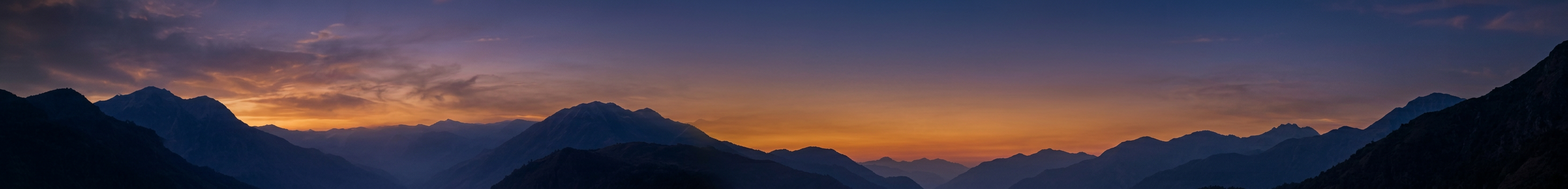 Layered mountain silhouettes beneath a dusk sky with an amber horizon
